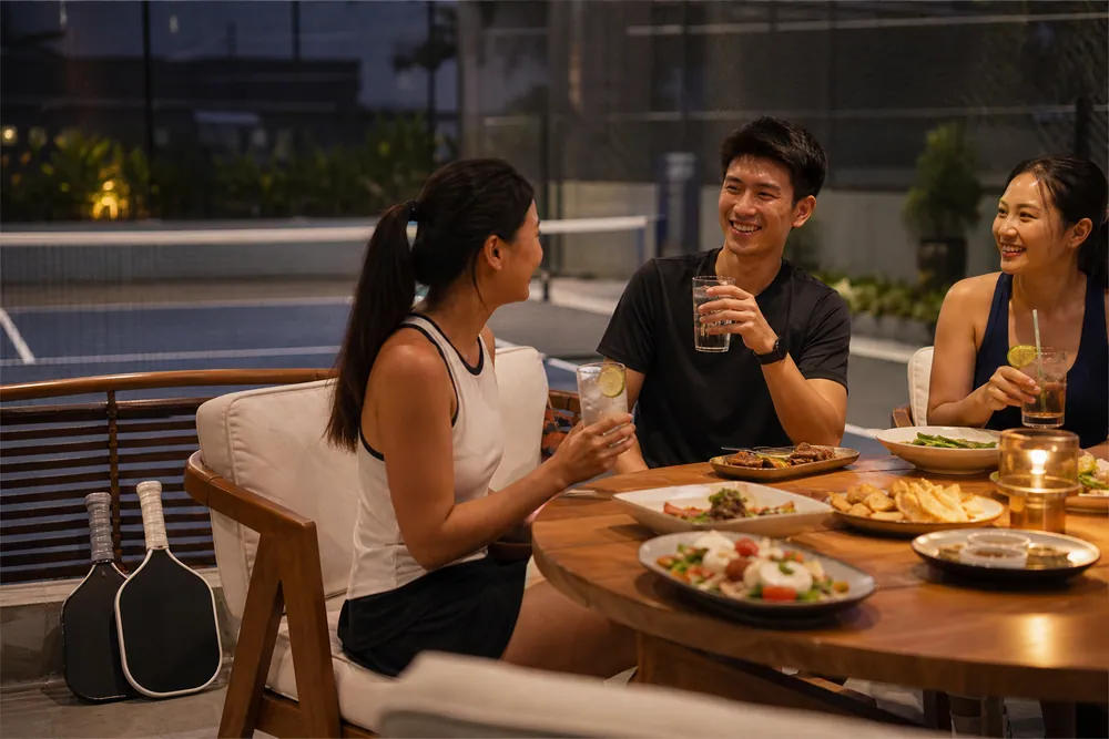 Friends sharing food and drinks beside a pickleball court after playing.